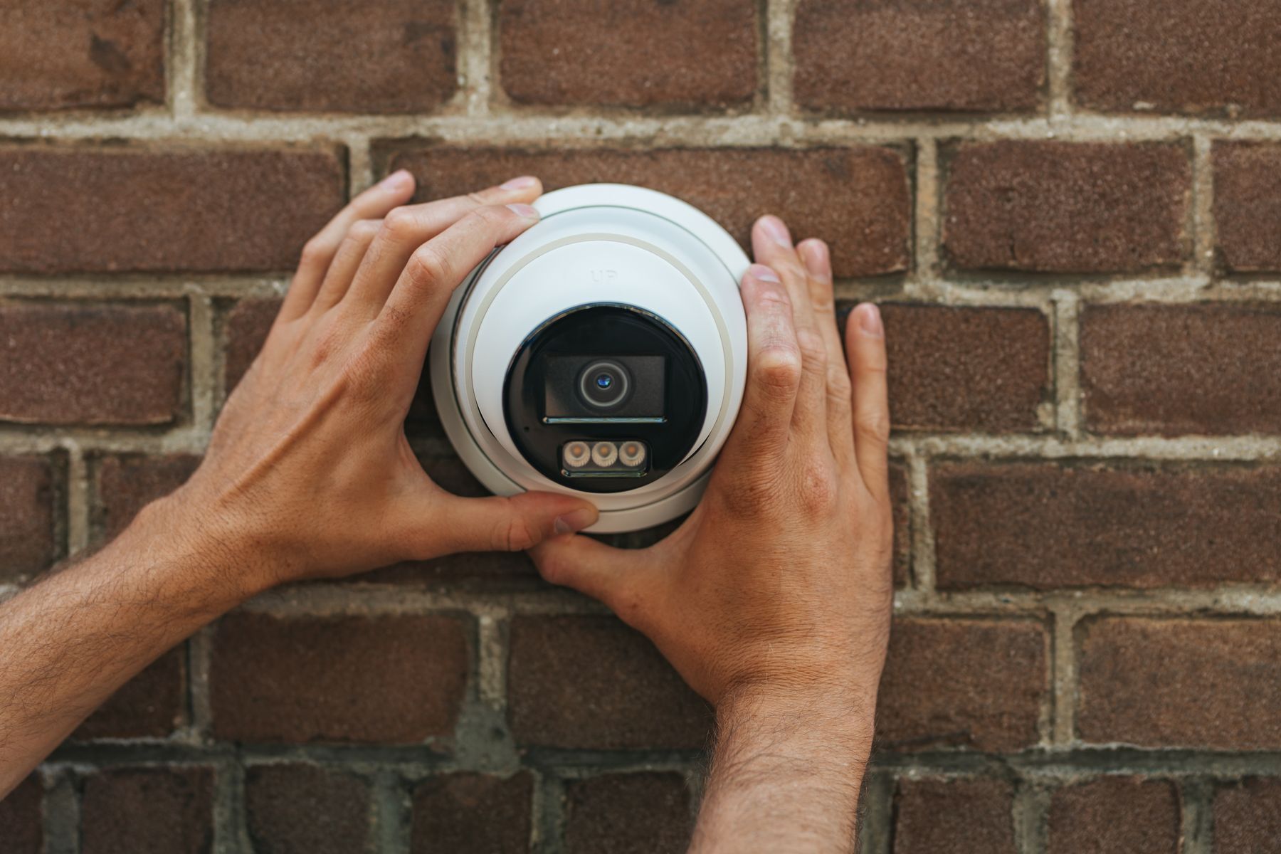 Handen van een monteur zetten een Hikvision-camera vast op een bakstenen muur